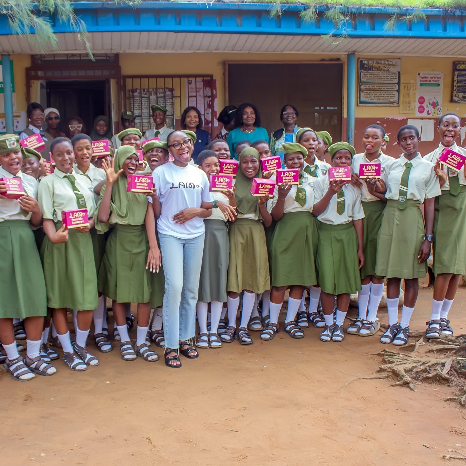 Group of students in green uniforms holding lam period cards pads with the founder in the center, standing in front of a school building.